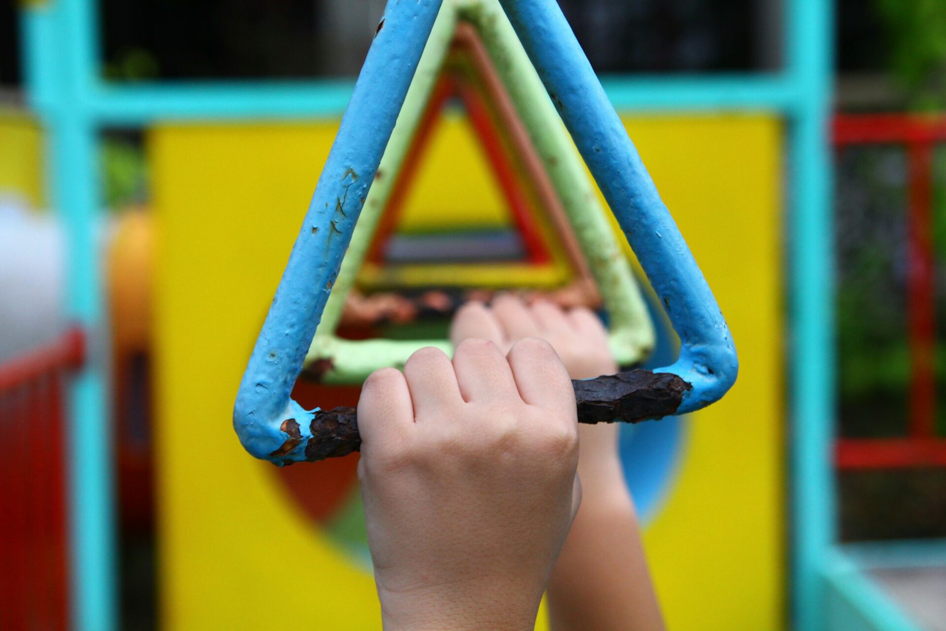 Close-up of child's hands gripping triangular jungle gym monkey bars in assorted colors.
