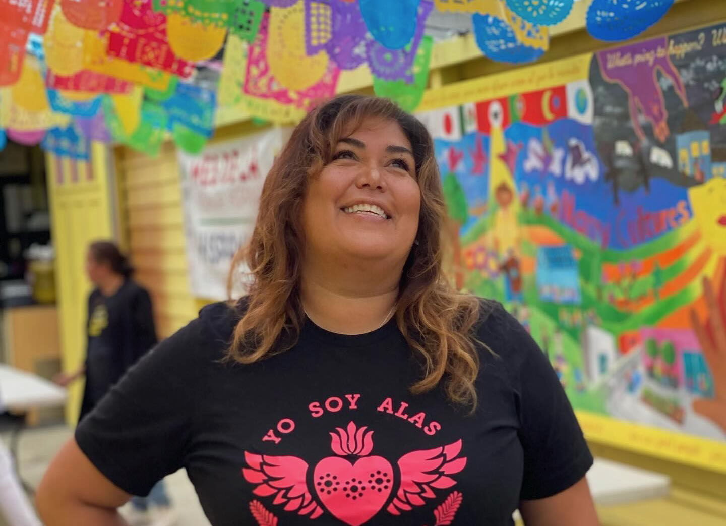 Woman in black shirt with red writing that says "yo soy ALAS"