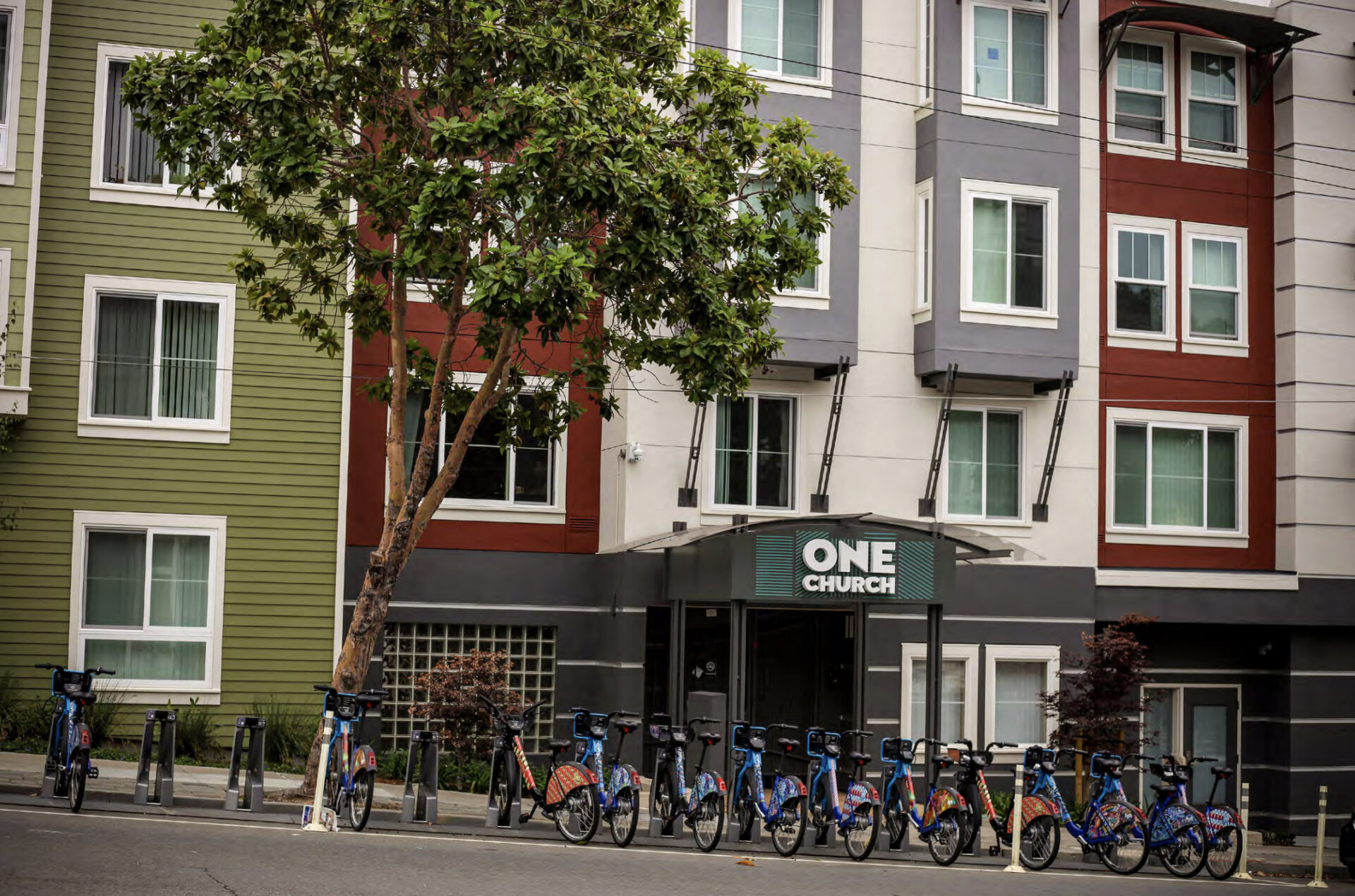 The red, white and gray facade of an affordable housing development, with bikeshare docks in front