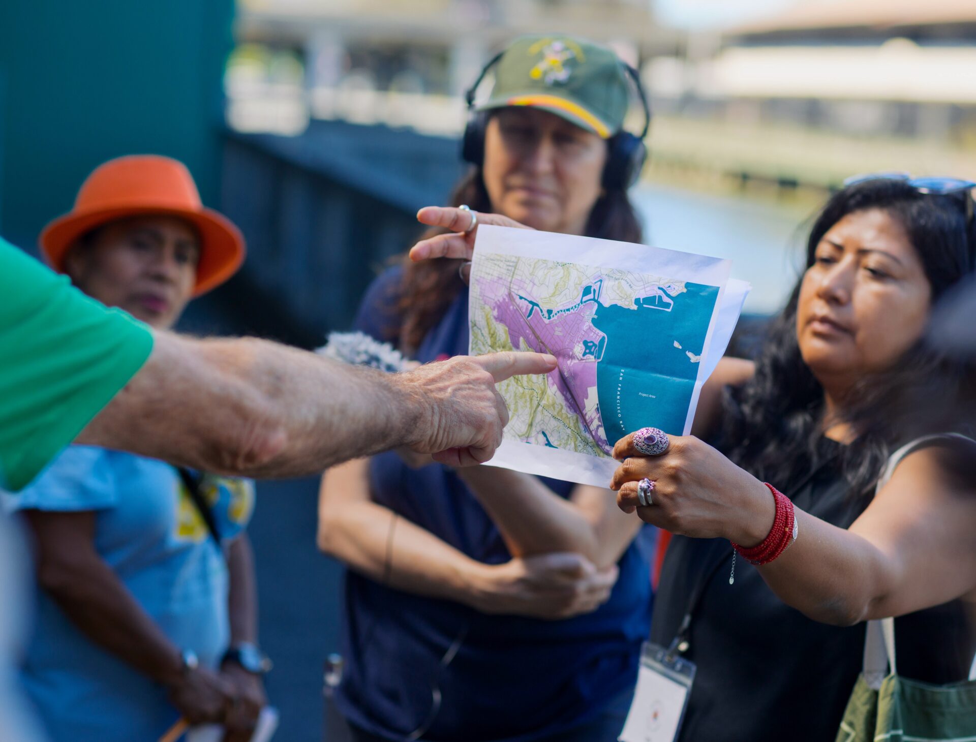 A woman holds up a map of Bay Area sea level rise as someone in front of her out of frame points to part of the map.