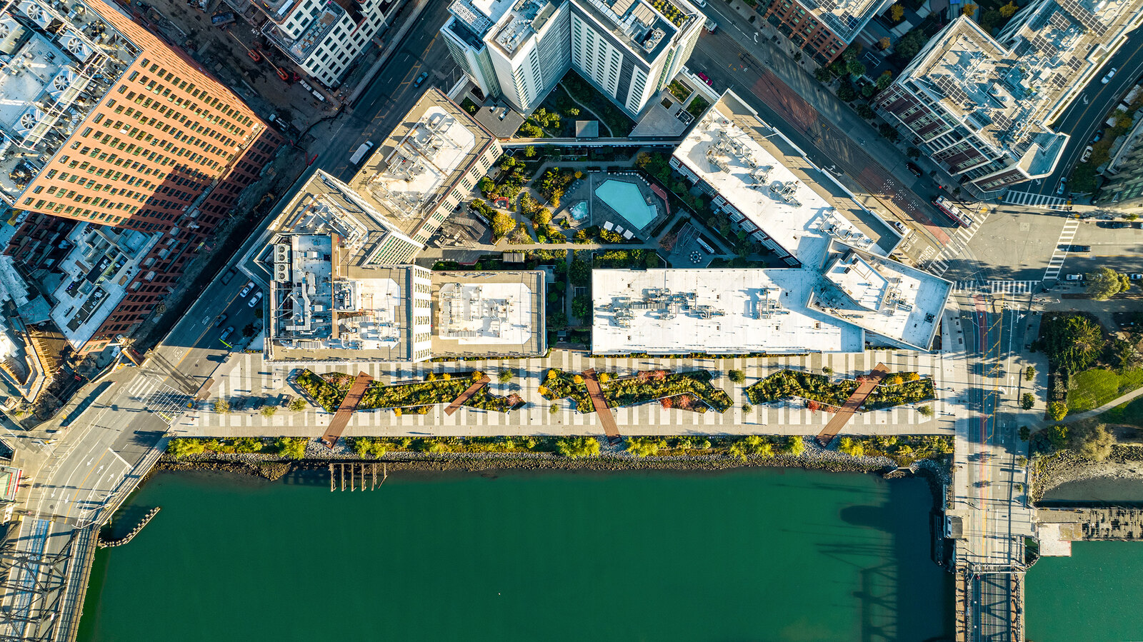A bird's-eye view of an urban walkway/park in the center, with Mission Creek pictured below and buildings pictured above