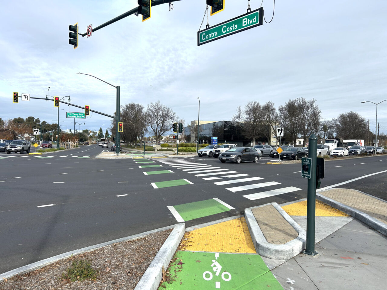 Newly painted pedestrian and bike lanes through an intersection, with traffic signals above and a green street sign marking the road as Contra Costa Boulevard