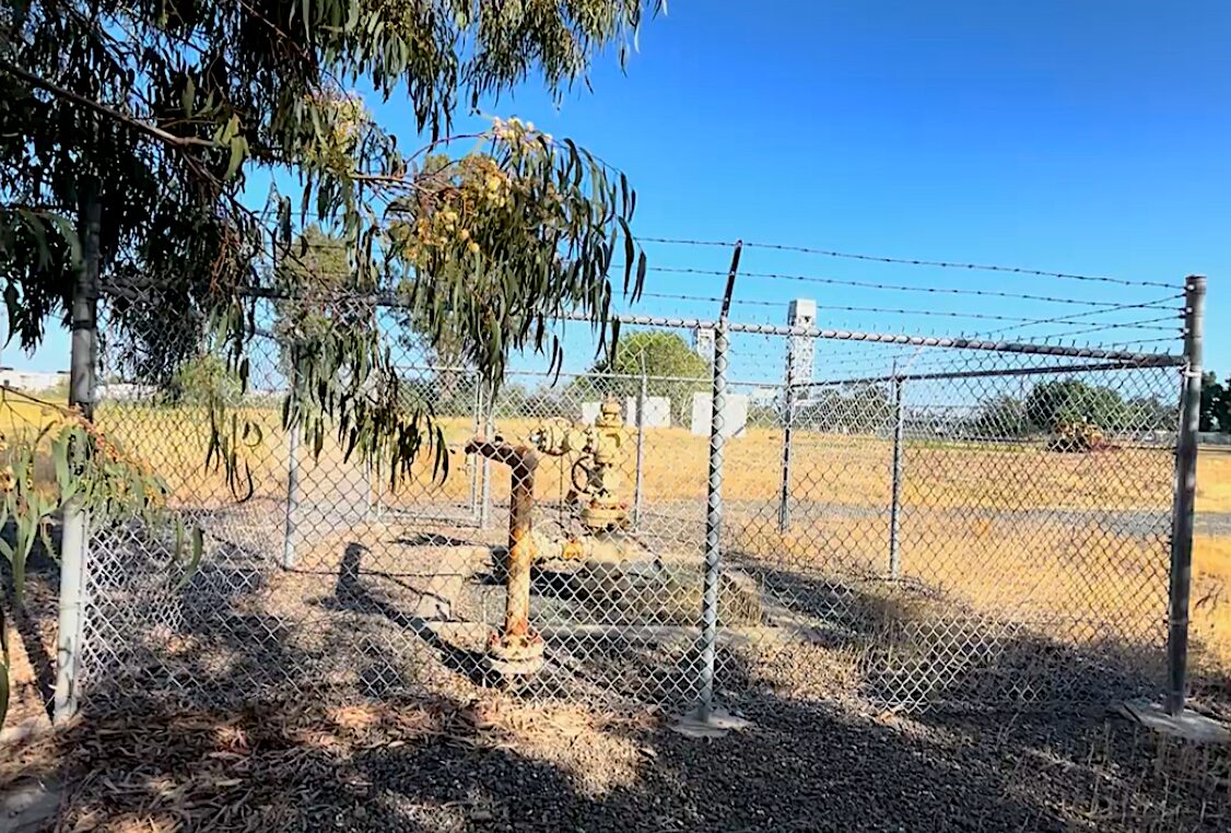 Gas well visible behind a chain-link fence.
