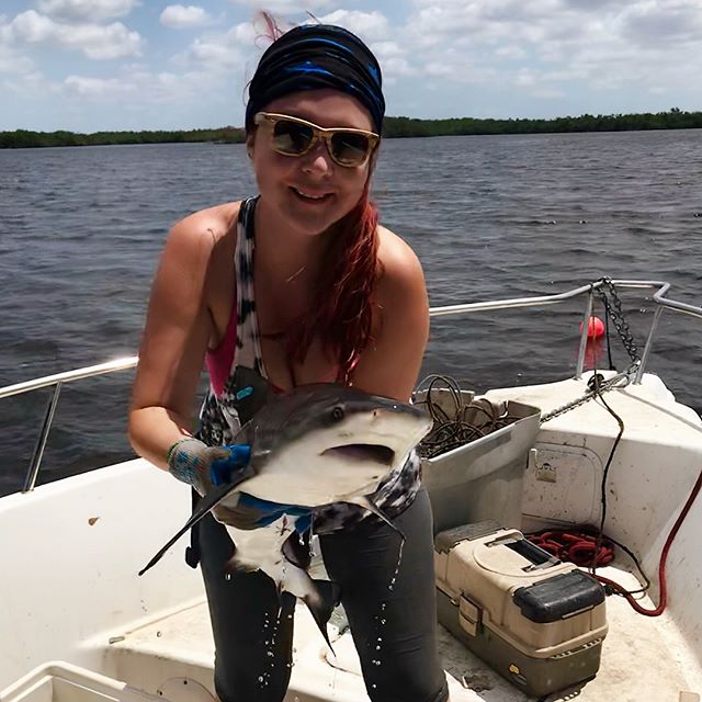 Camila C&aacute;ceres stands on a boat, holding a small shark. 