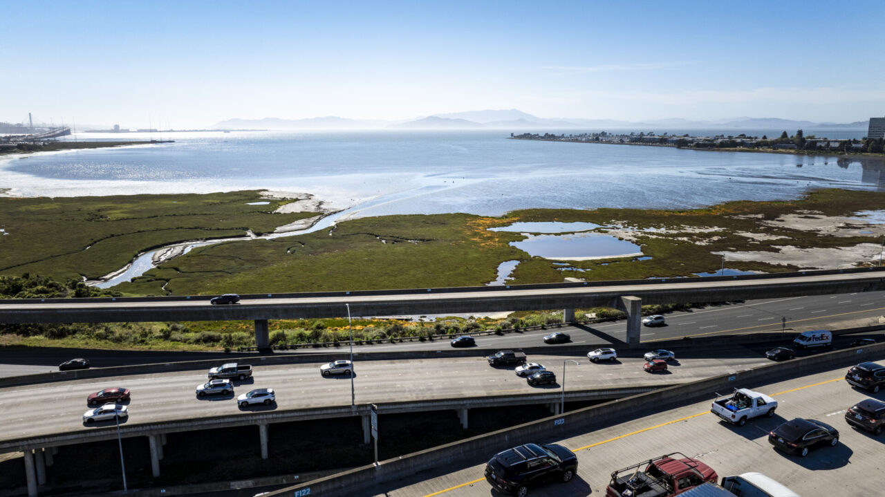 A wide view of the Bay in the background, with the highway in the foreground and a marsh in between.