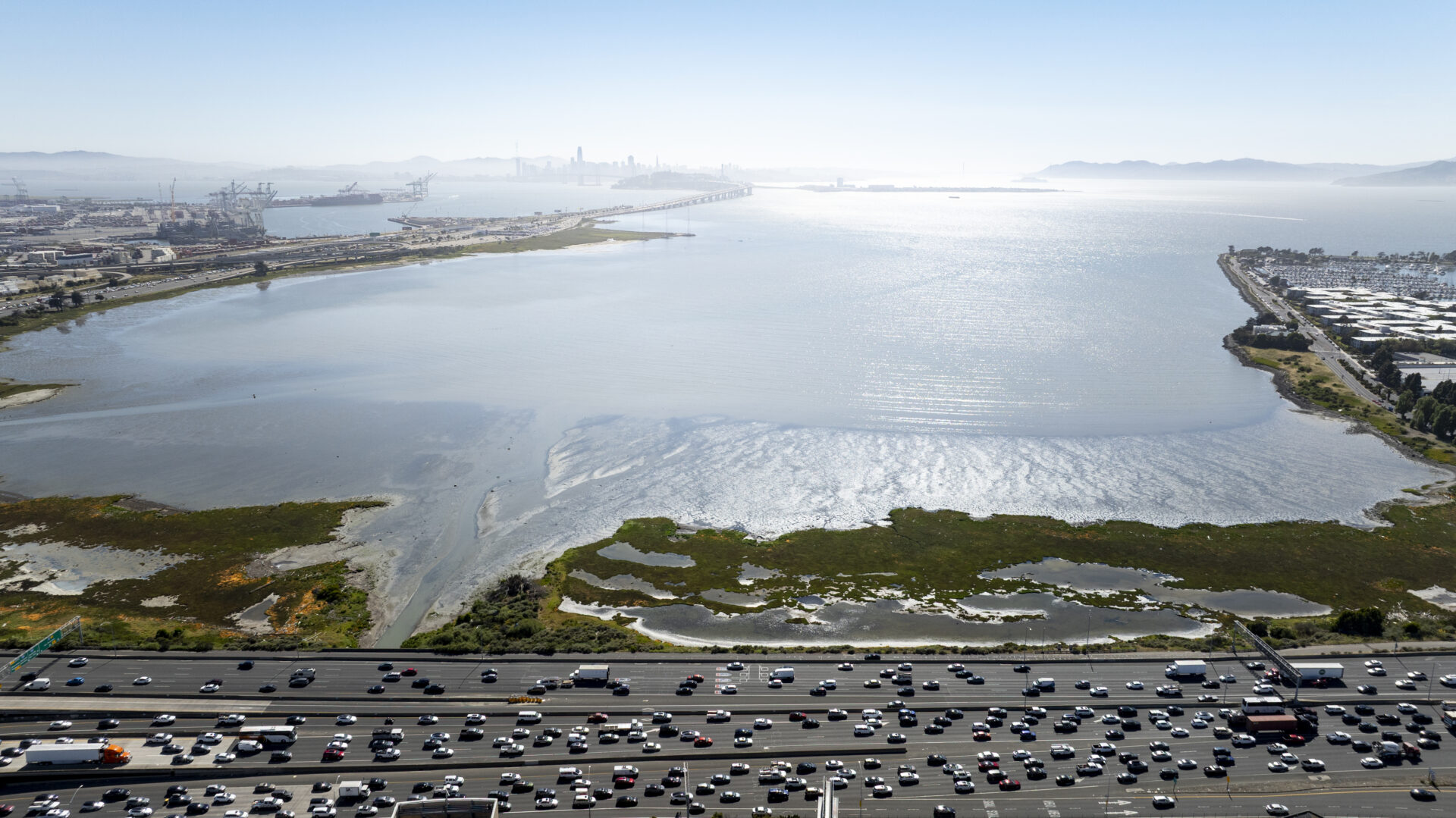 A wide view of the Bay in the background, with the highway in the foreground and a marsh in between.