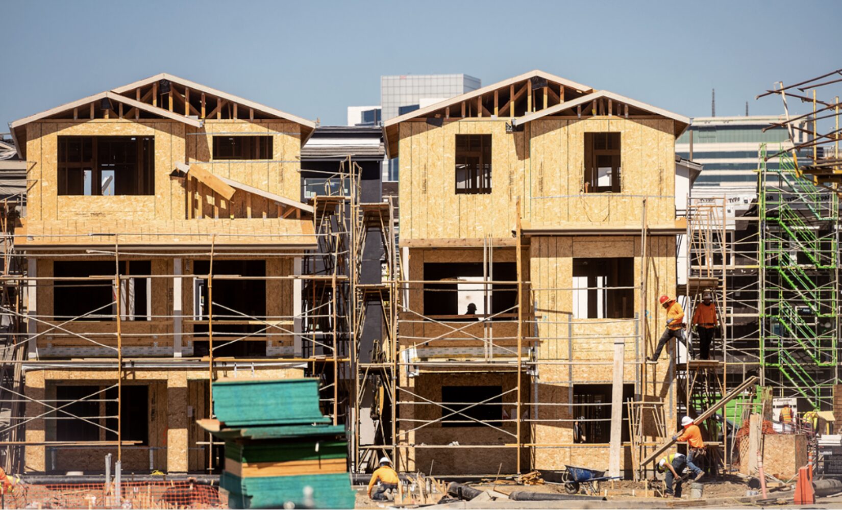 Two three-story multifamily residences under construction with main frames and wood visible
